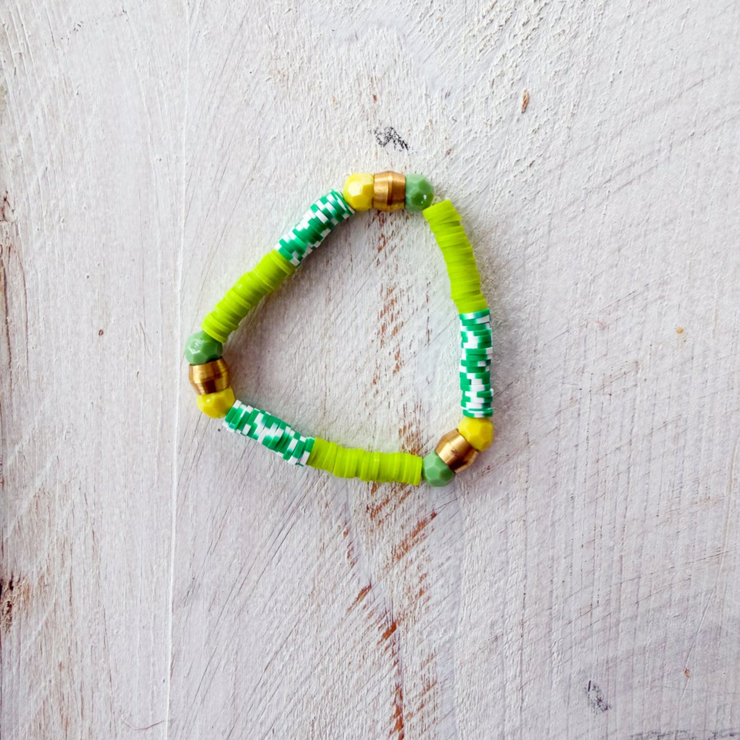 Green beaded bracelet with gold accents on a light wooden surface