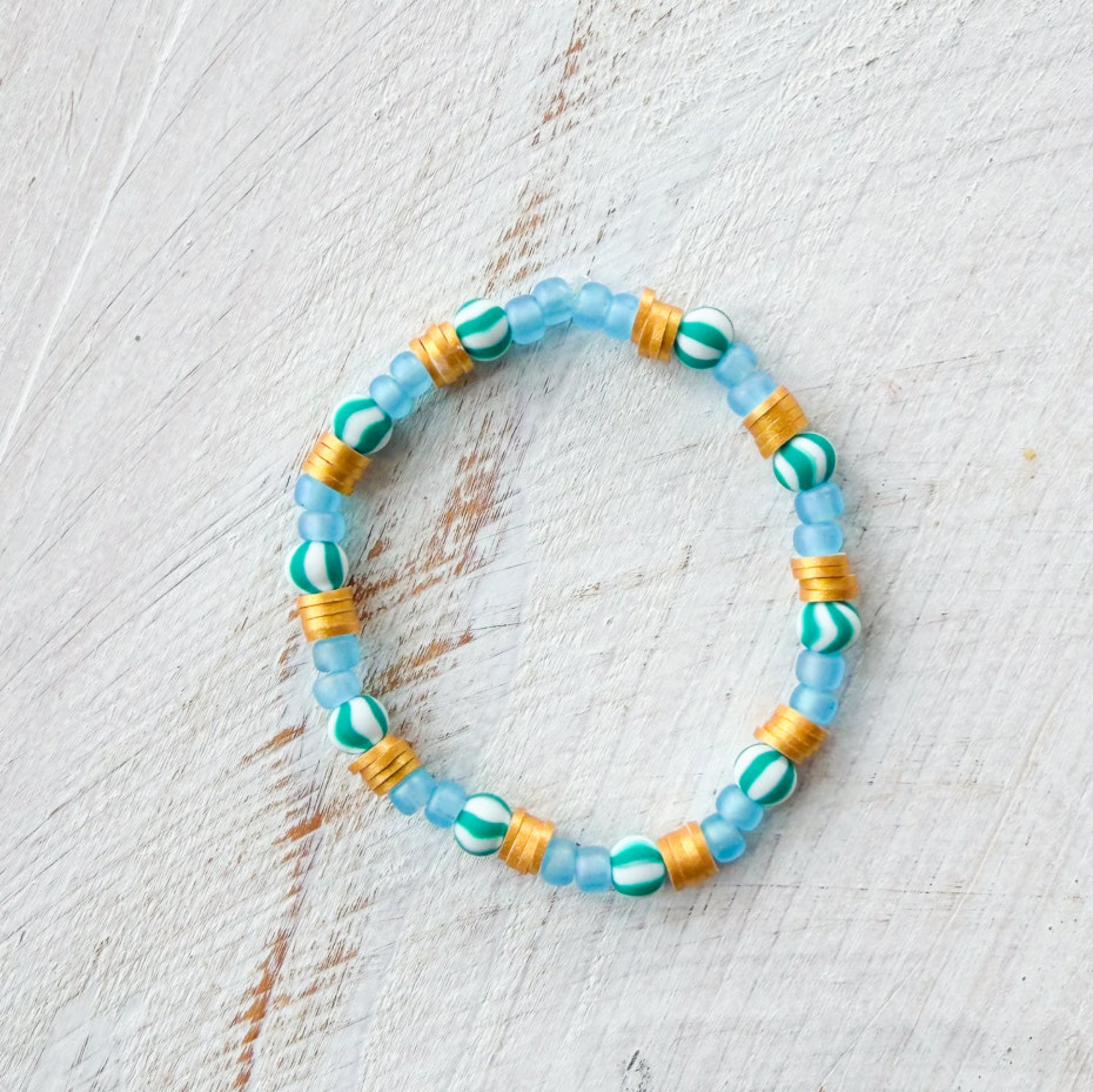 Beaded bracelet with blue, green, and gold beads on a light wooden surface