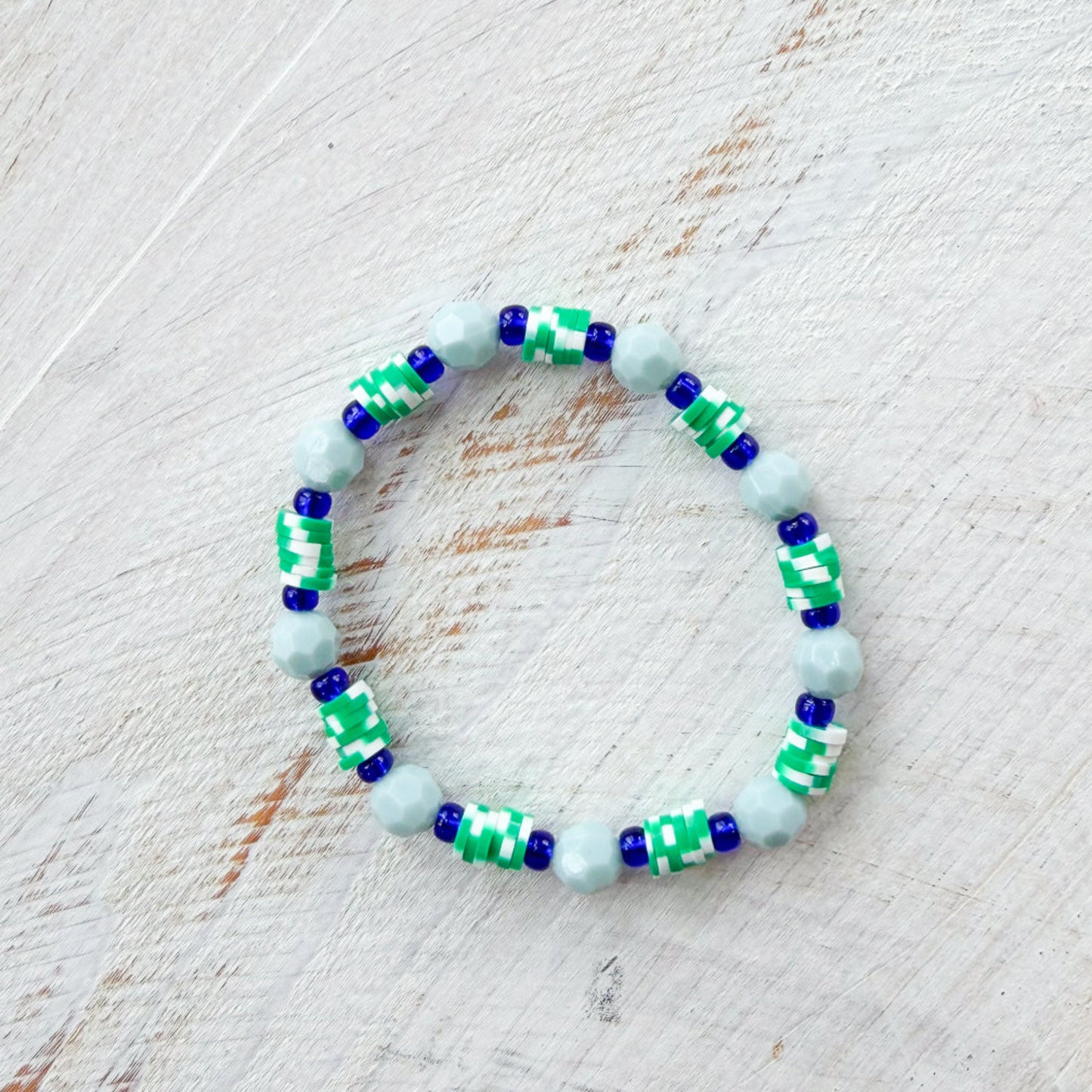 Beaded bracelet with green and blue pattern on a light wooden surface