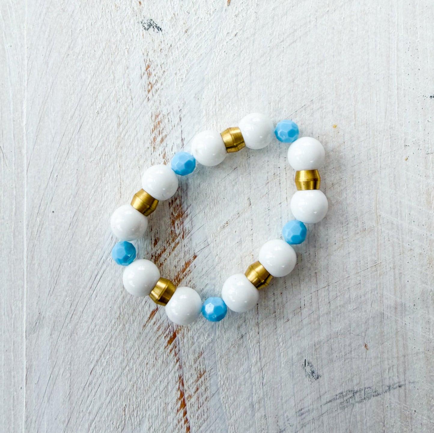 Beaded bracelet with white, gold, and blue beads on a light wooden surface
