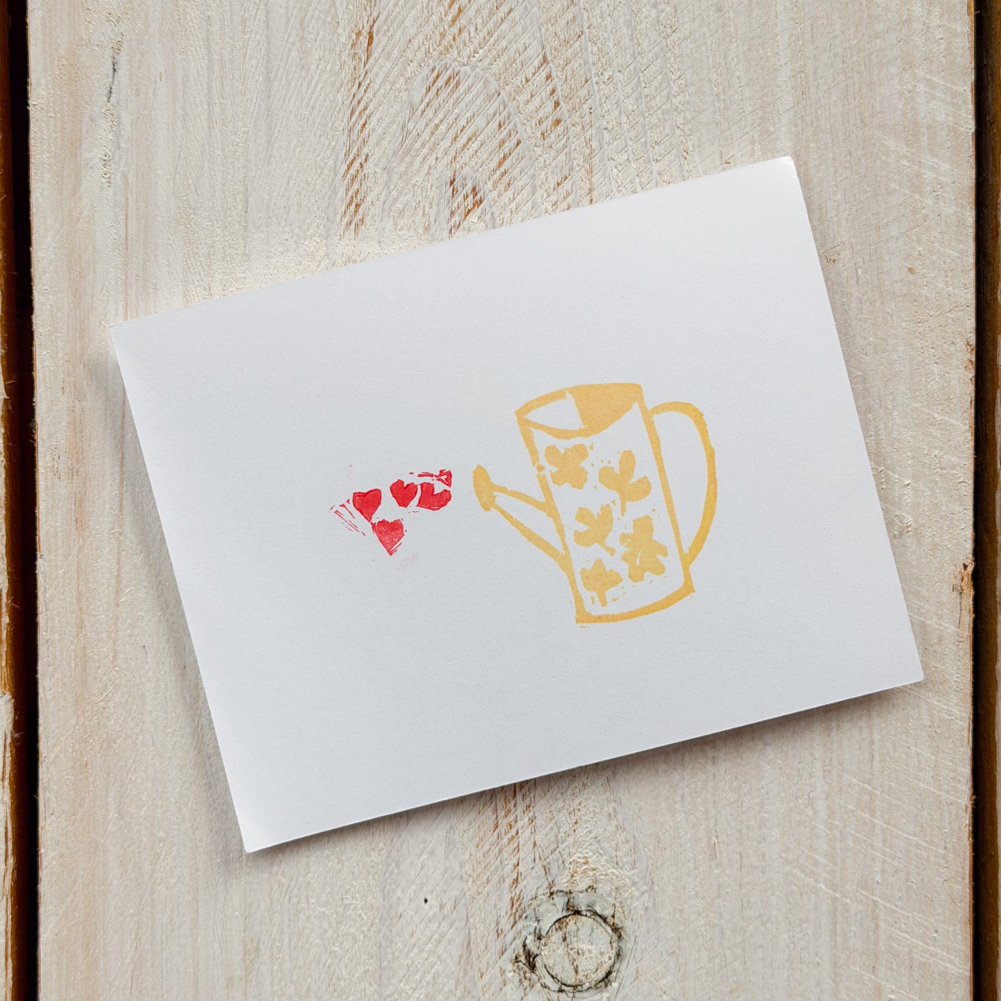 White card with a yellow watering can and red hearts stamp on paper