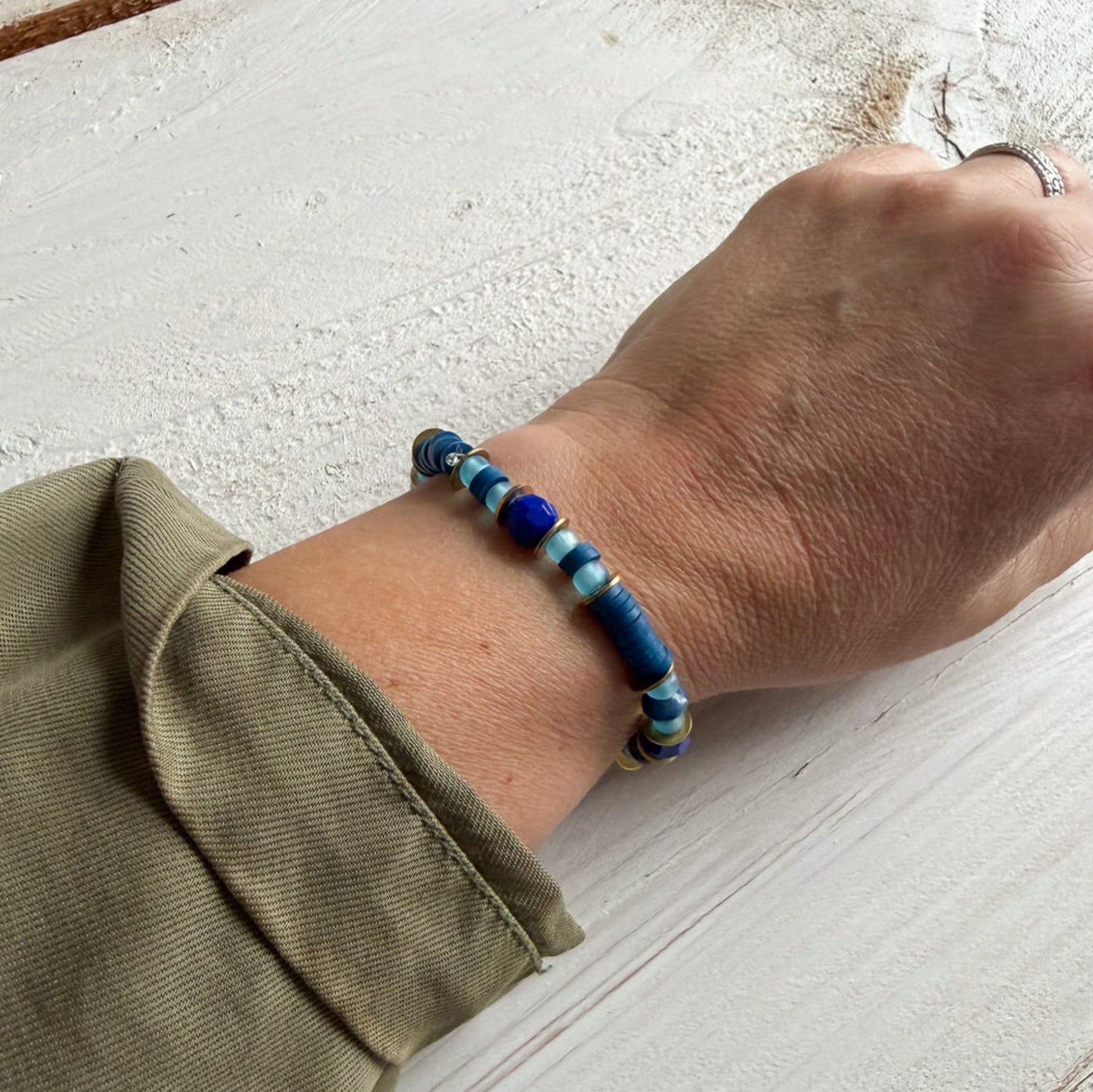 Hand wearing a blue beaded bracelet on a light surface
