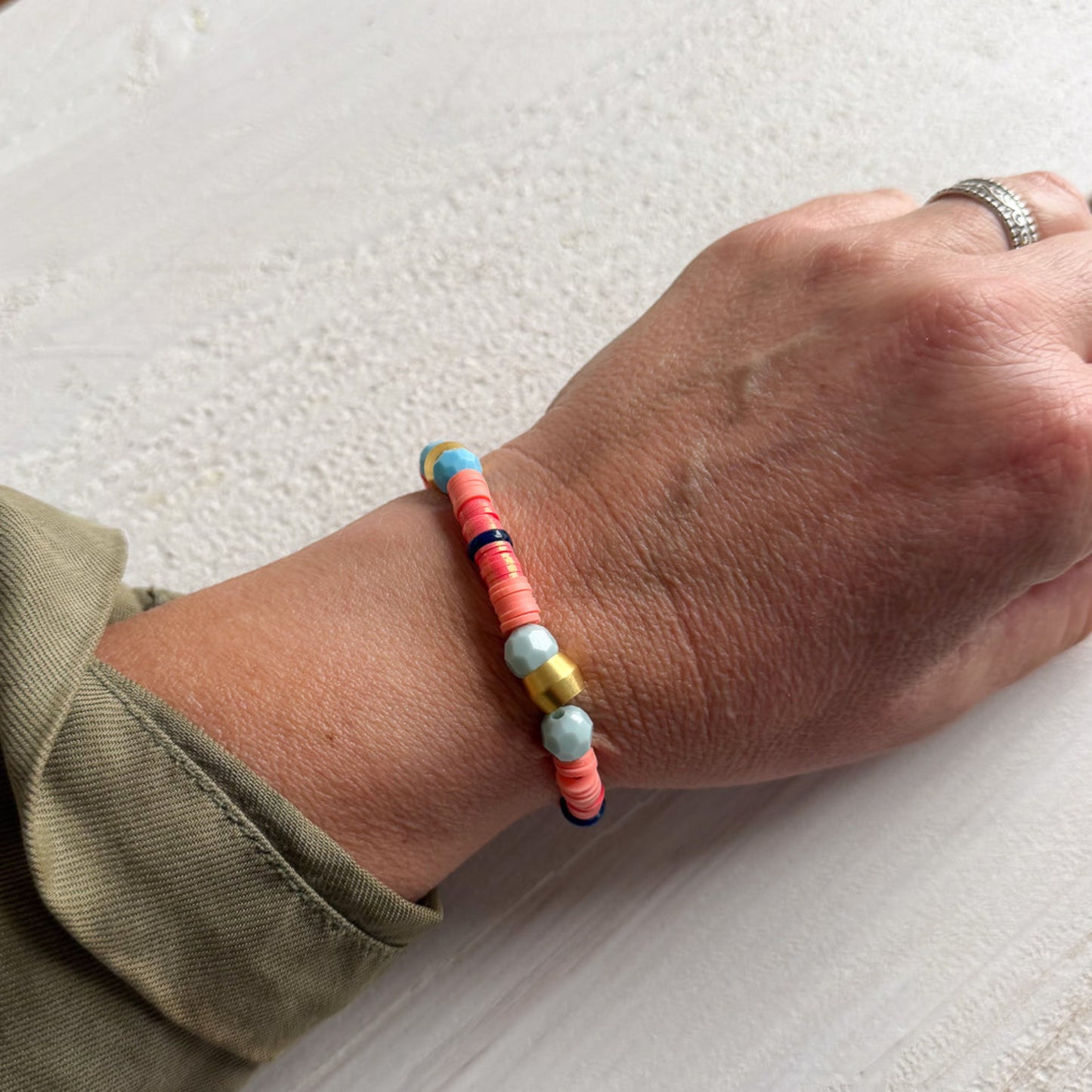 Hand wearing a colorful beaded bracelet on a textured surface