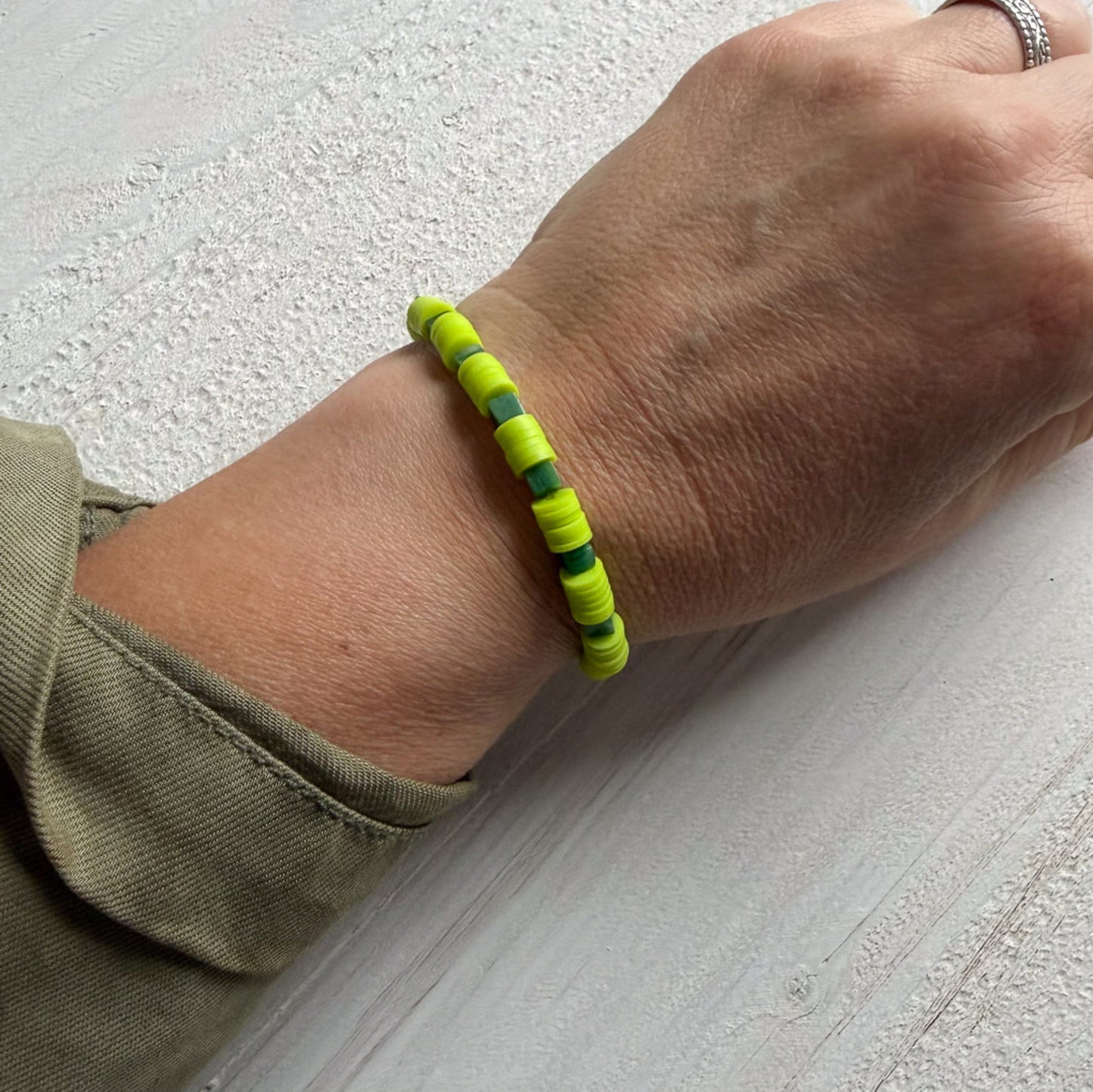 Hand wearing a green beaded bracelet on a light gray surface