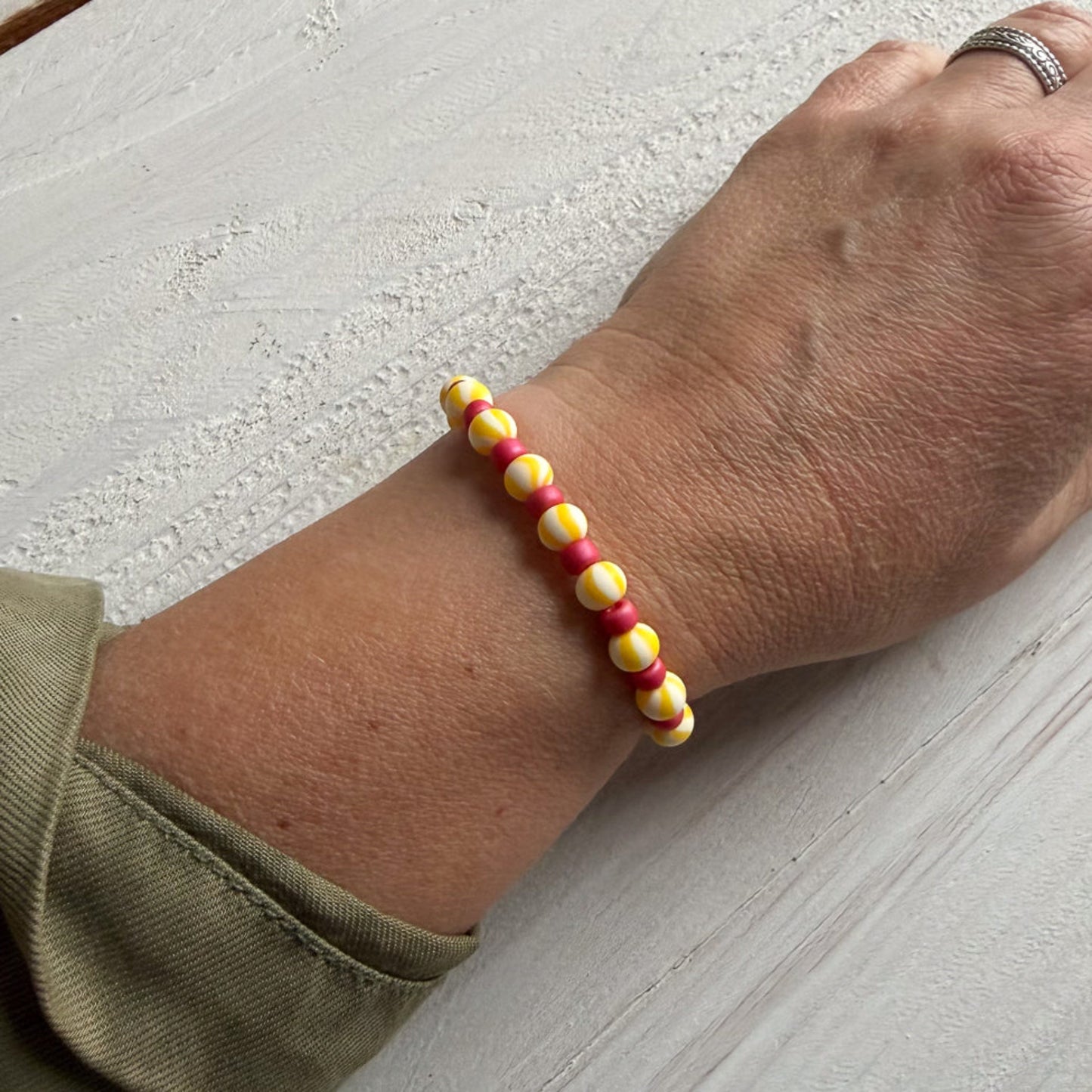 Hand wearing a colorful beaded bracelet on a light wooden surface
