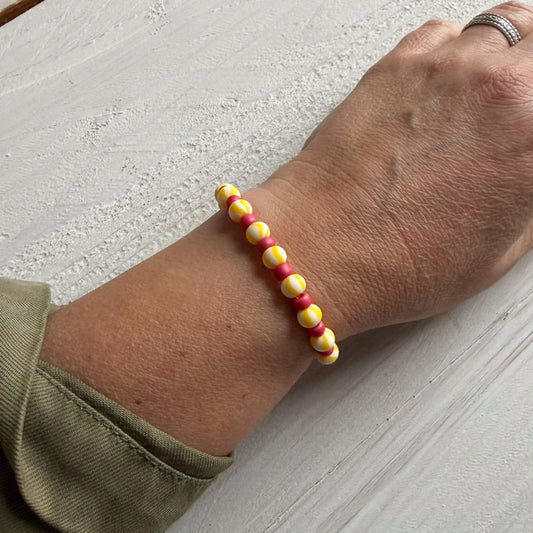 Hand wearing a colorful beaded bracelet on a light wooden surface