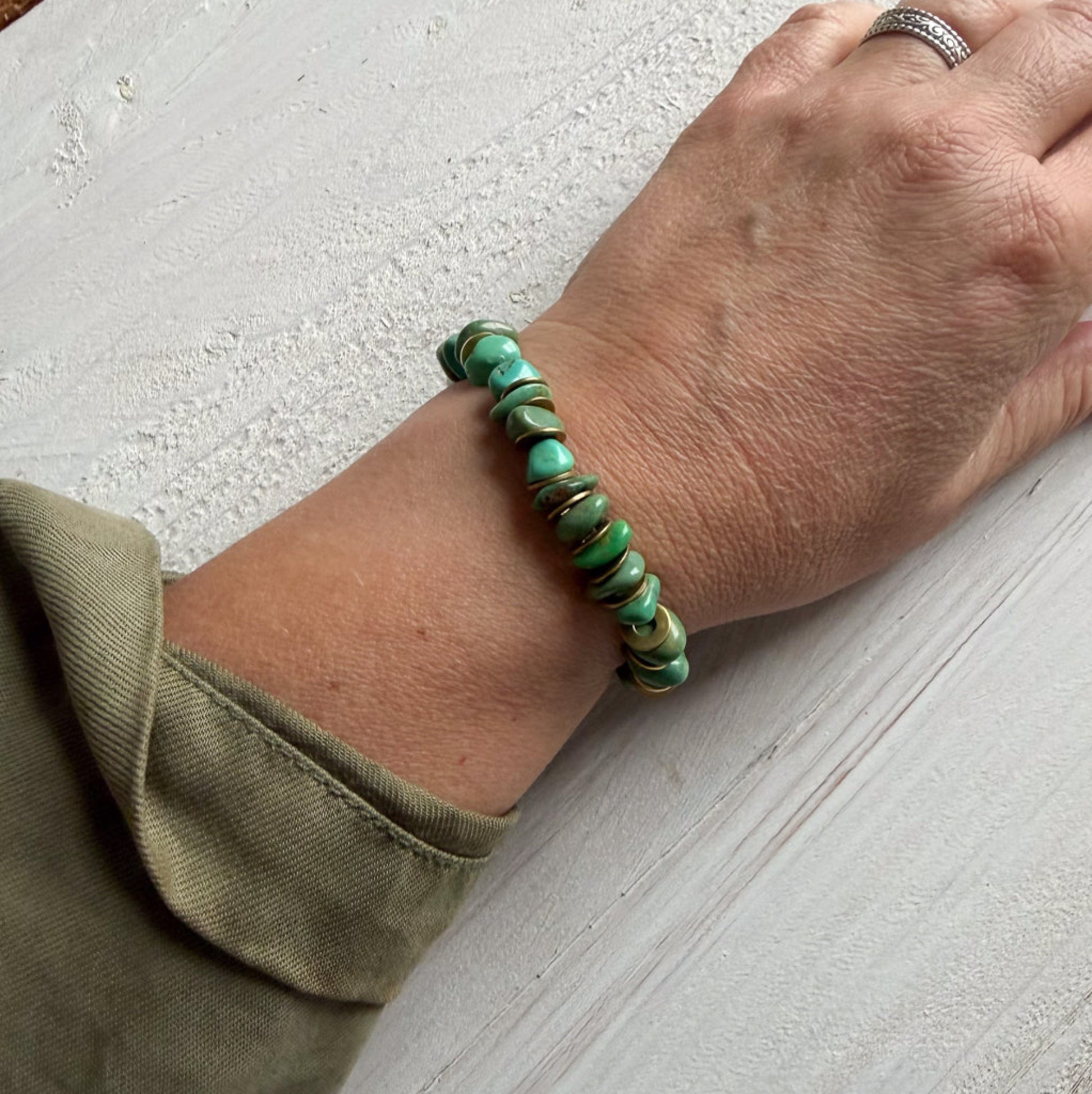 Hand wearing a green beaded bracelet on a light surface