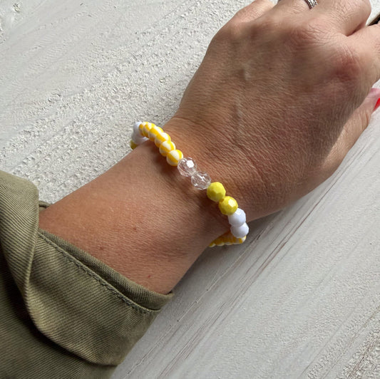 Hand wearing a bracelet with yellow, white, and clear beads on a light gray surface.