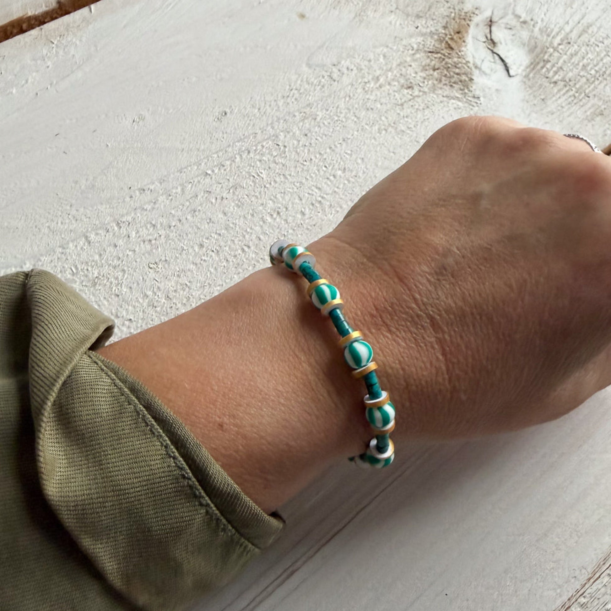 Hand wearing a turquoise beaded bracelet on a light wooden surface