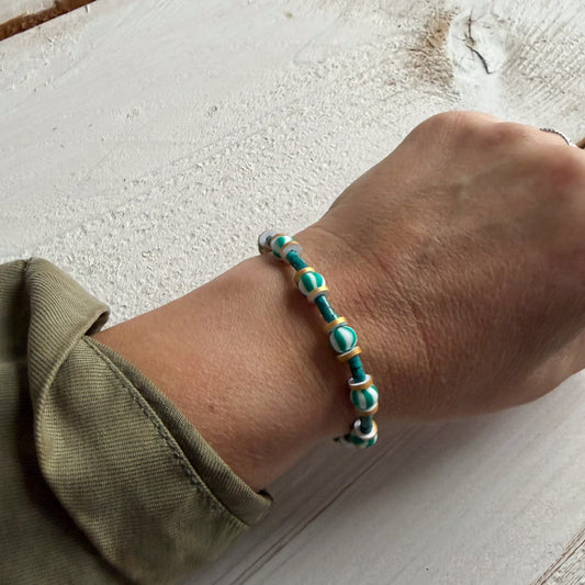 Hand wearing a turquoise beaded bracelet on a light wooden surface