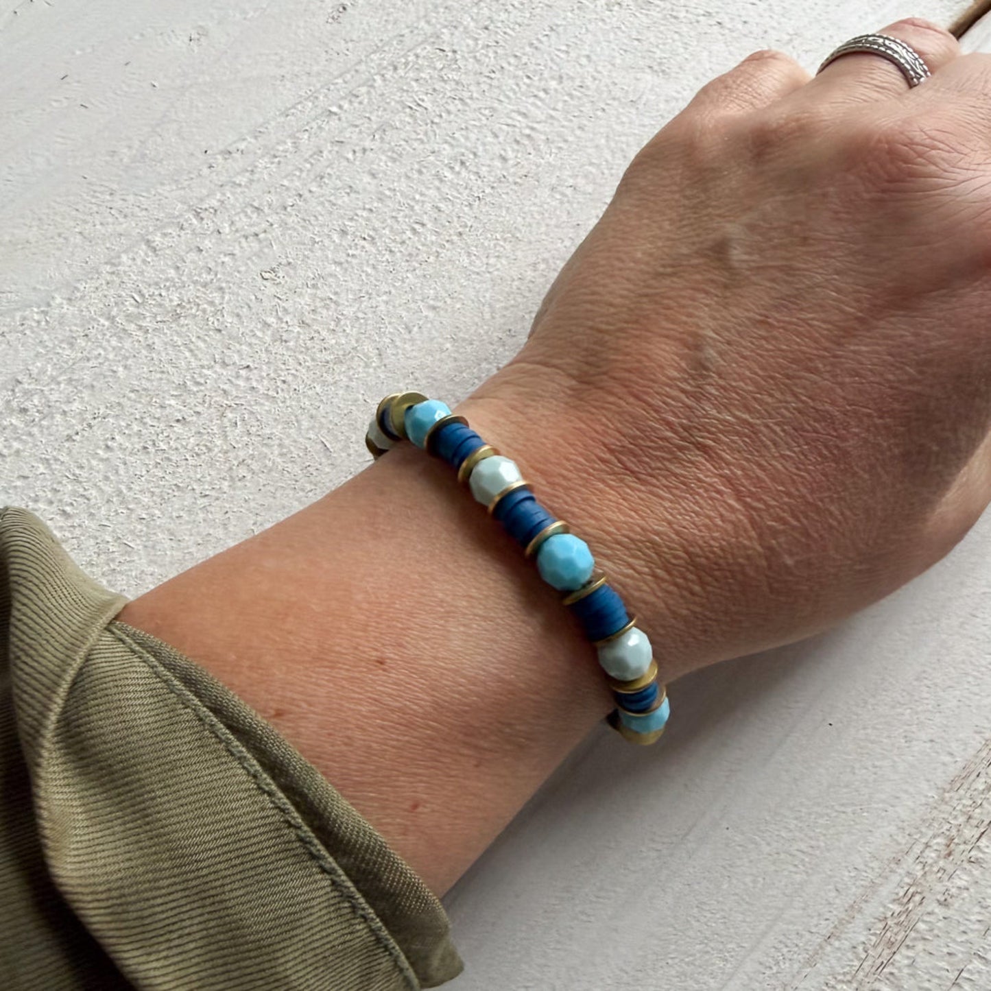 Hand wearing a beaded bracelet with blue, white, and gold beads on a light background