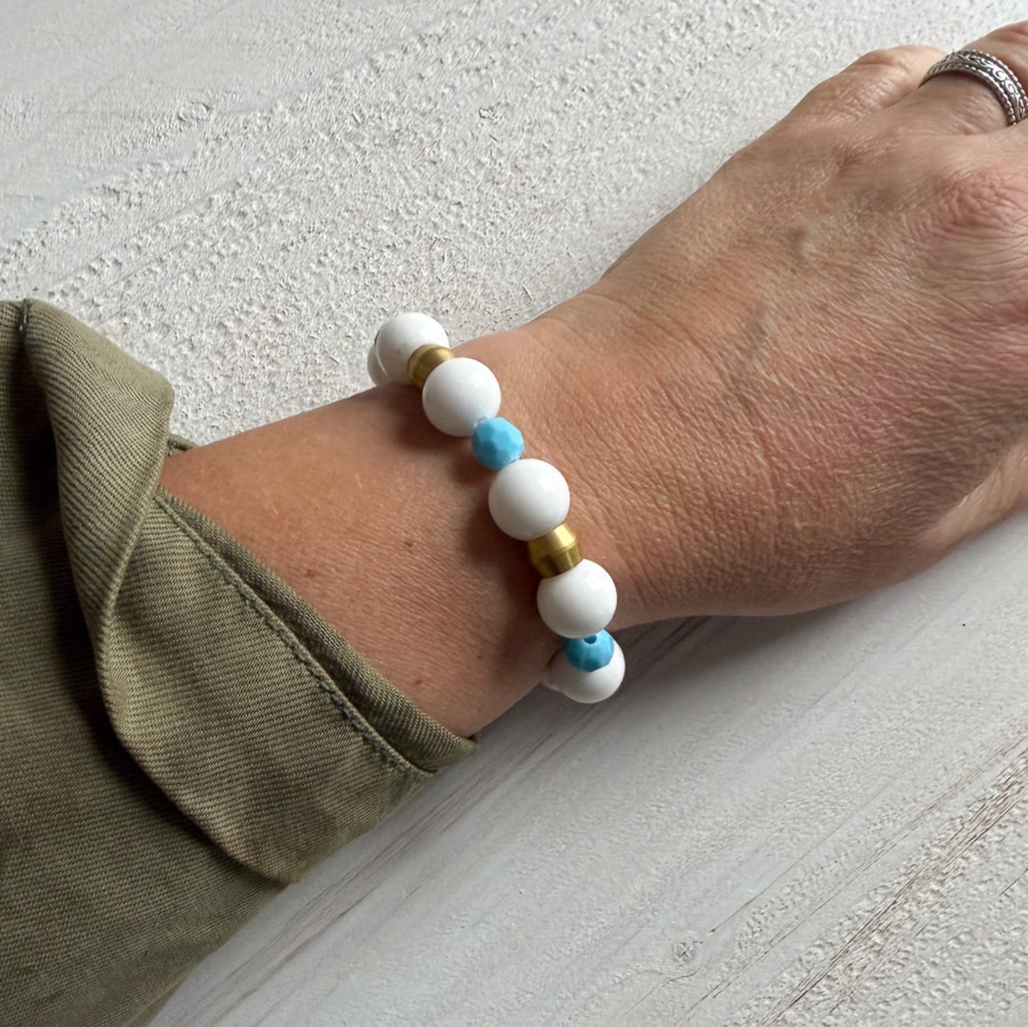 Close-up of a wrist wearing a bracelet with white, blue, and gold beads on a light background.