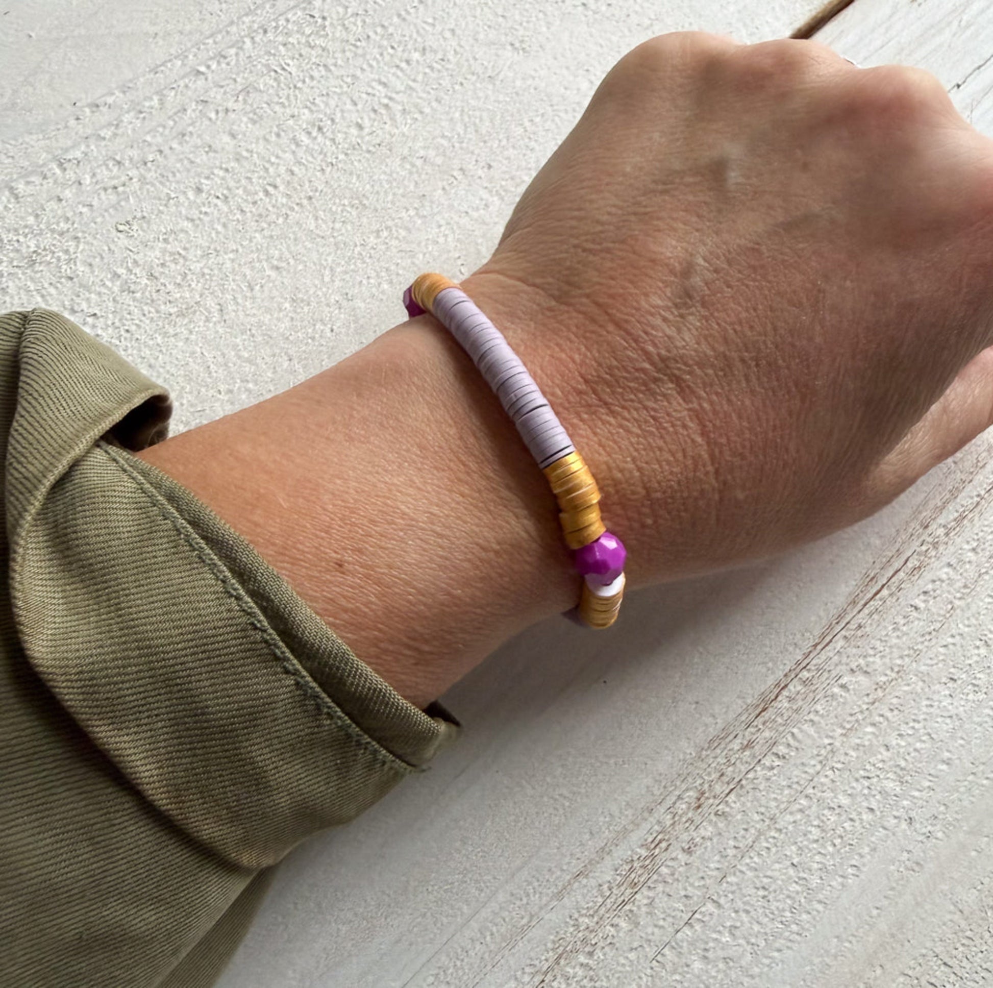 Hand wearing a bracelet with purple and gold beads on a light gray surface