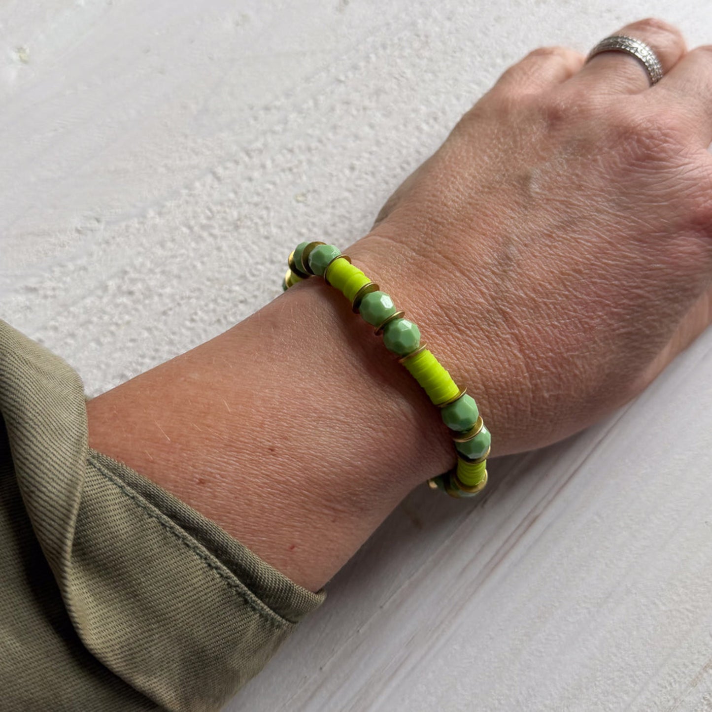 Hand wearing a green beaded bracelet on a light background