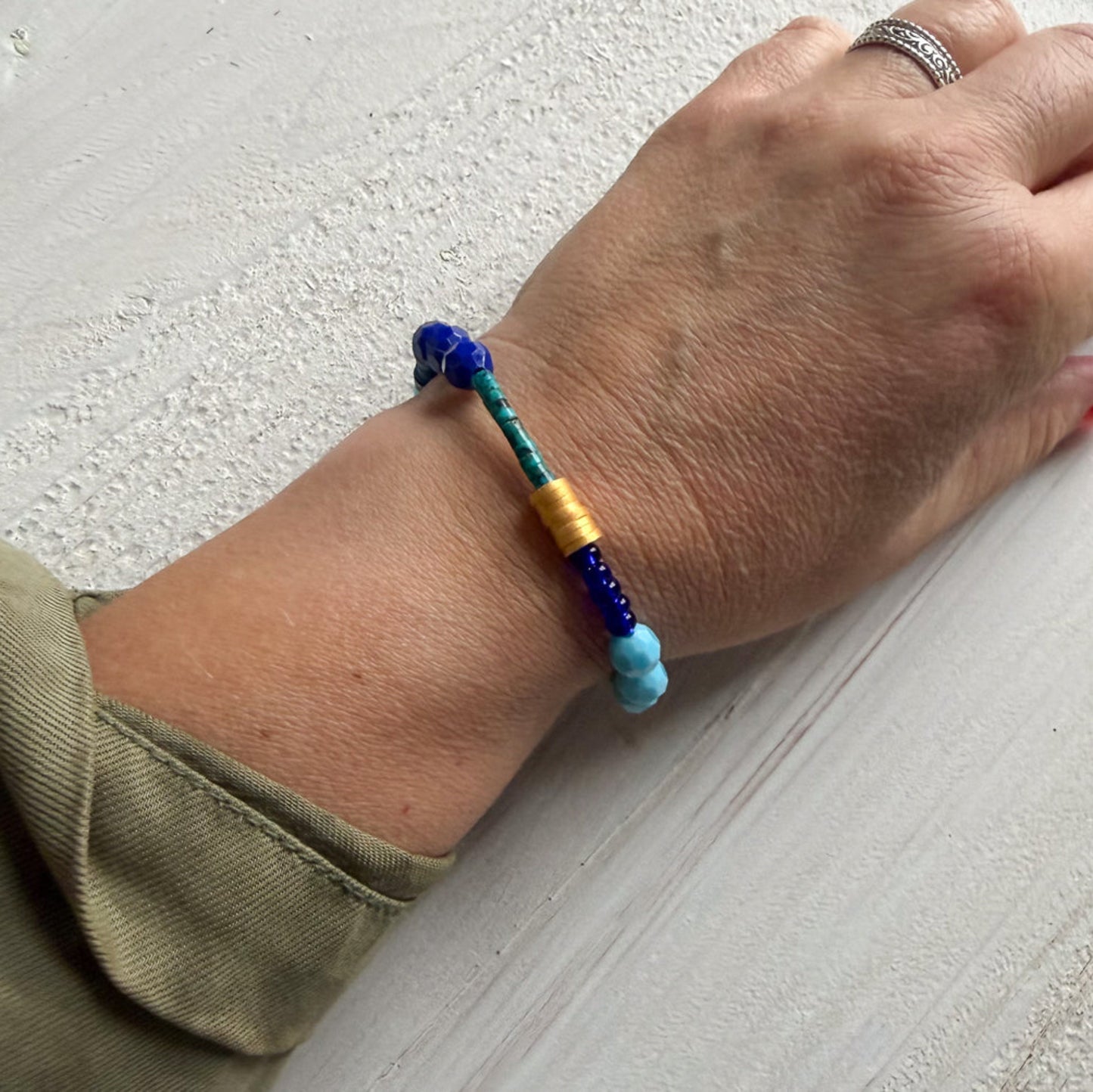 Hand wearing a colorful beaded bracelet on a light gray surface